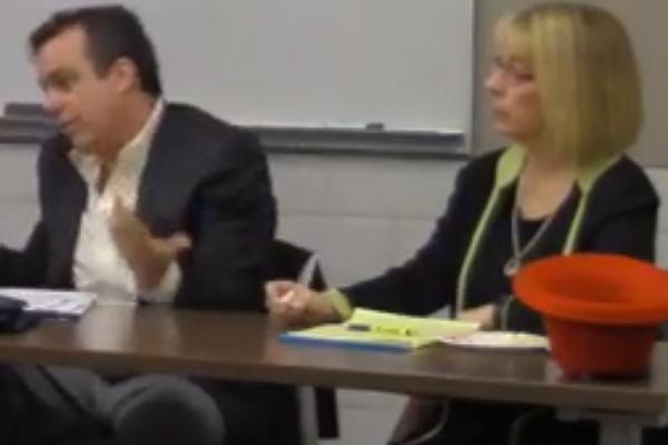 A man with short dark hair sits next a woman with blonde hair while speaking