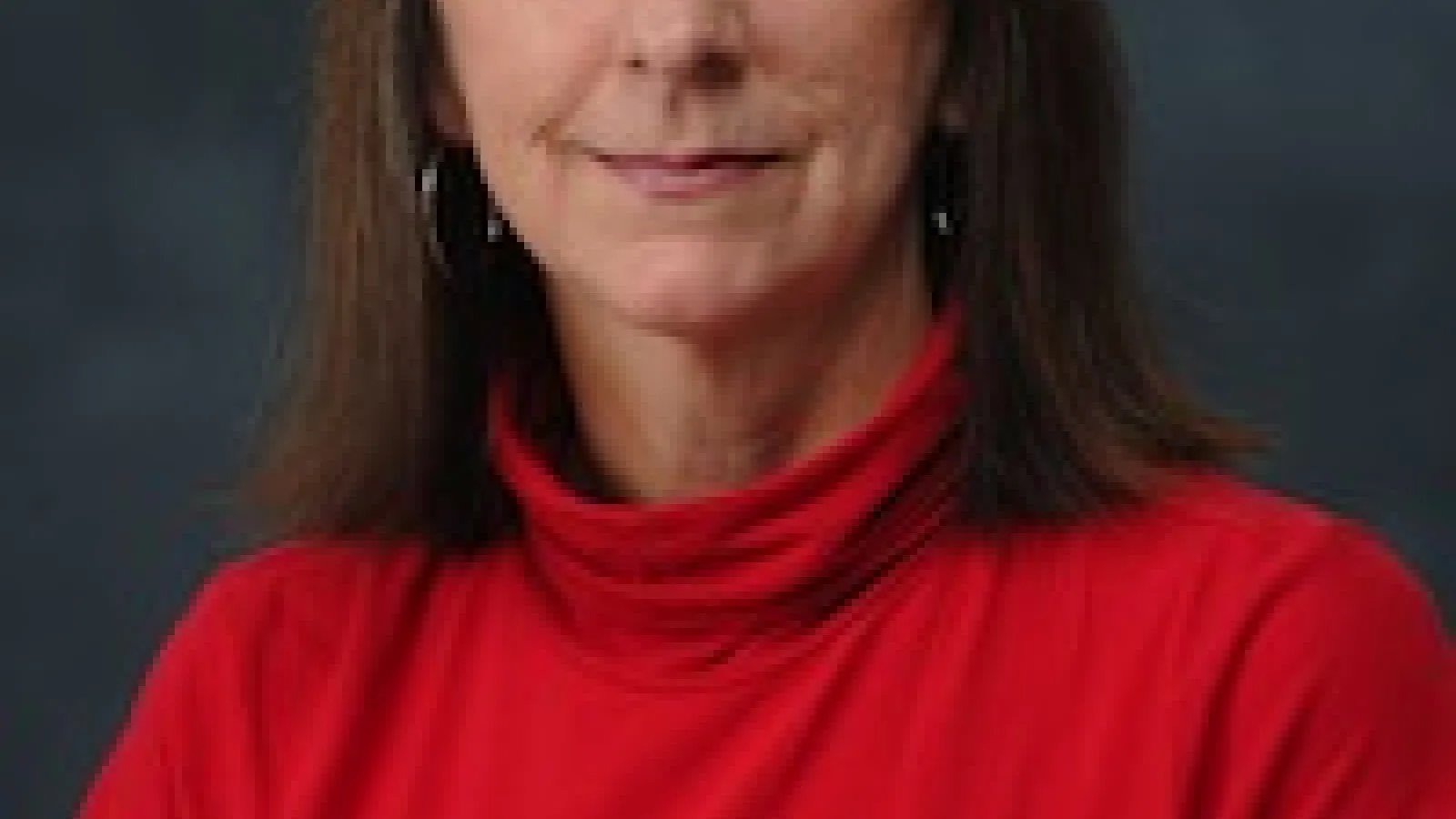 A light skinned woman with dark brown hair and an orange shirt looks at the camera
