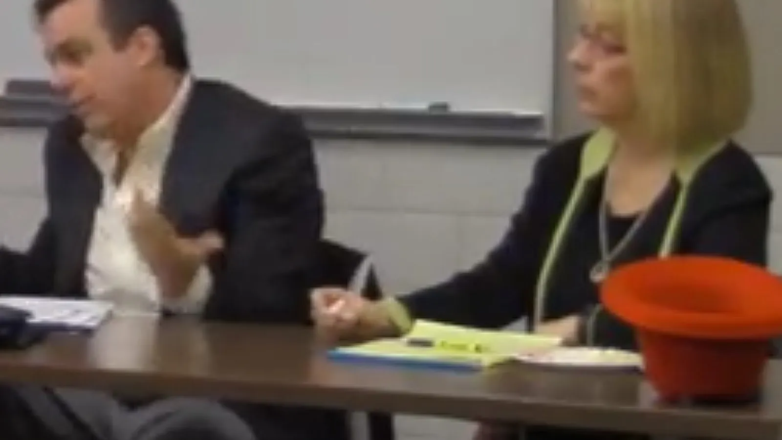 A man with short dark hair sits next a woman with blonde hair while speaking