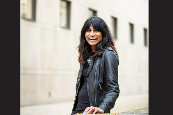 A woman wearing a leather jacket with long brown hair, she is smiling