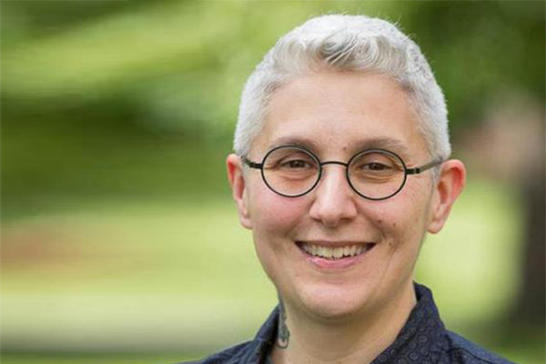 Woman with short grey hair and round glasses smiling at camera
